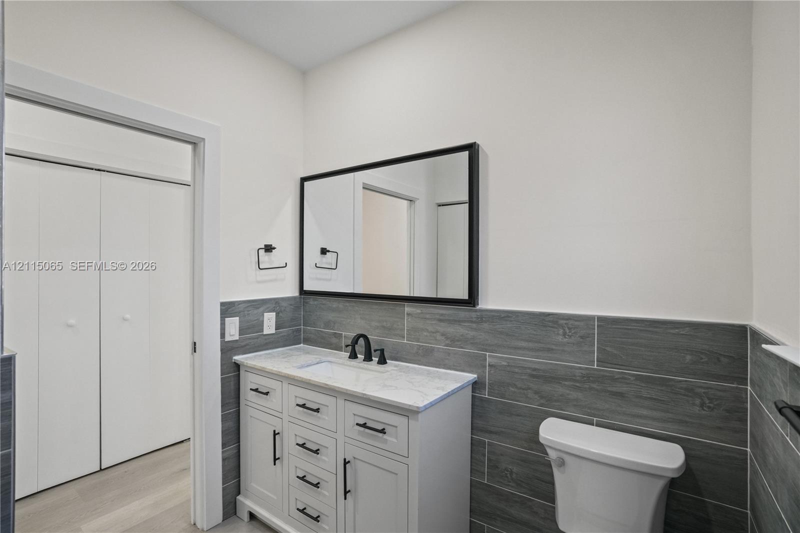 Bathroom featuring a white vanity with stone-top basin, matte black hardware, rectangular mirror, and gray horizontal wall tile