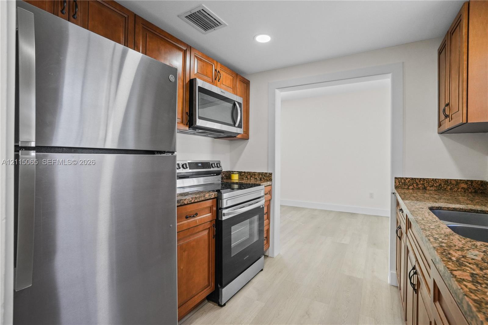 Kitchen featuring wood cabinetry, stone countertops, stainless steel appliances, and light-tone wood-finish flooring Kitchen featuring wood cabinetry, stone countertops, stainless steel appliances, and light-tone wood-finish flooring