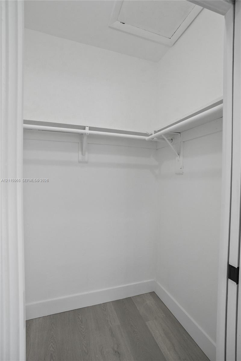 Storage space featuring wood-finish flooring and L-shaped shelving with integrated hanging rods