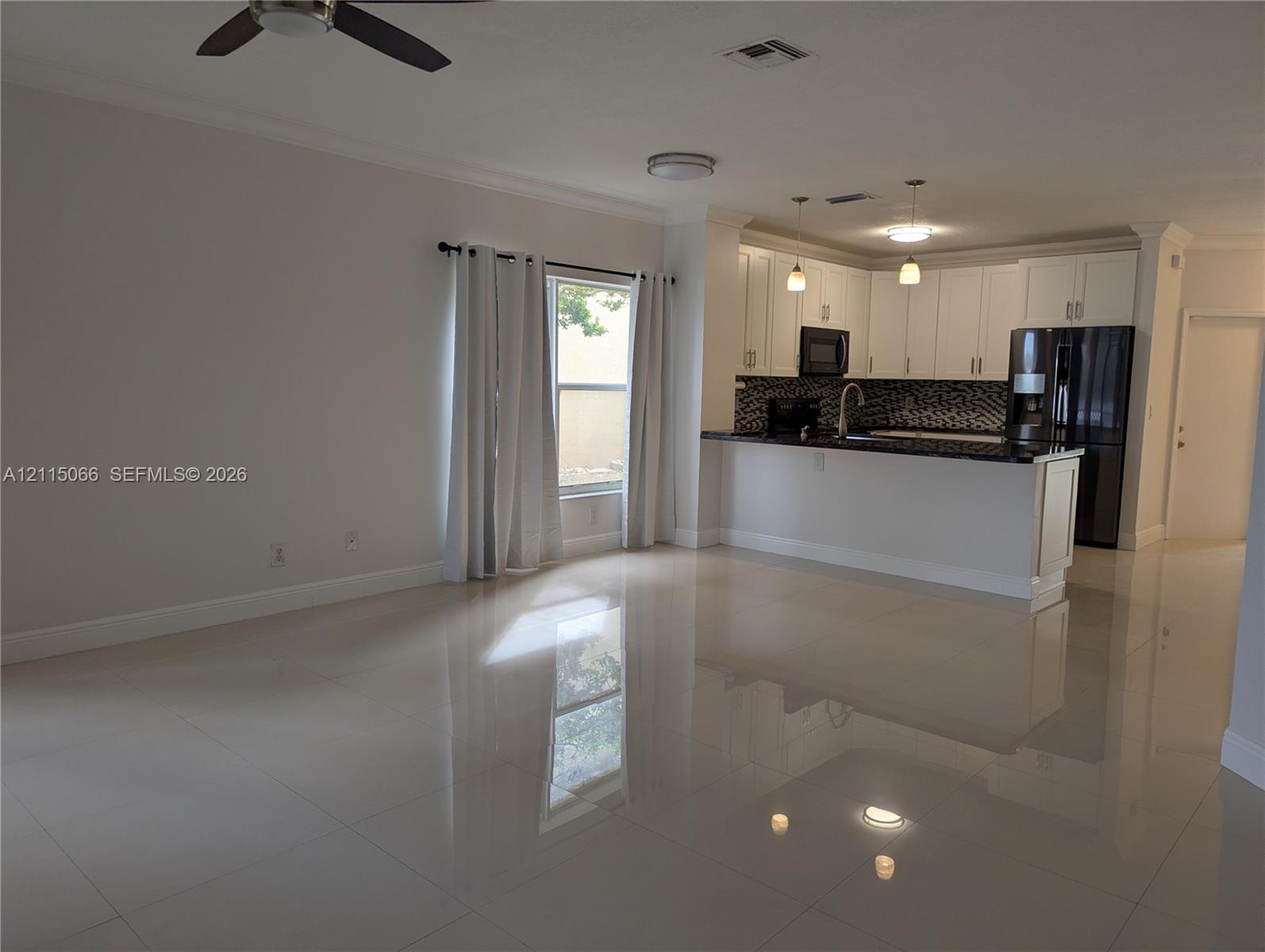 Open interior space featuring polished tile flooring, white cabinetry, a kitchen peninsula with dark stone countertops, mosaic tile backsplash, and recessed and pendant lighting
