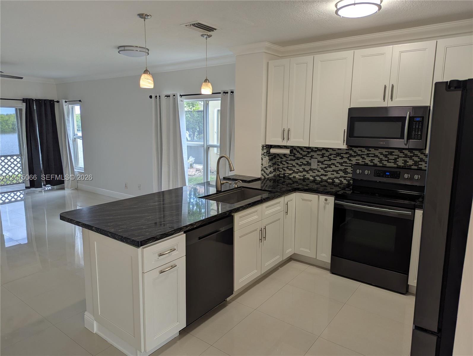 Kitchen featuring white shaker-style cabinetry, dark stone countertops, a mosaic tile backsplash, stainless steel appliances, and a central island with an integrated sink