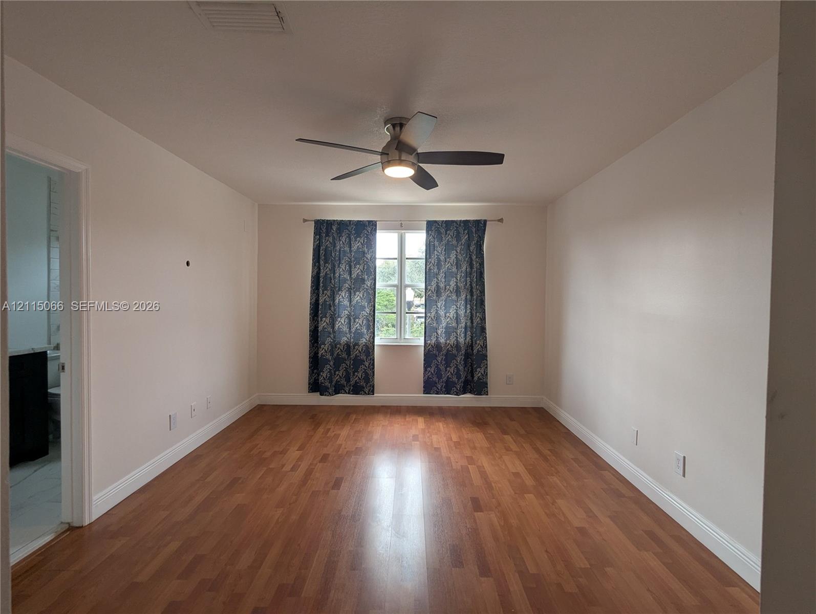 Interior space featuring wood-finish flooring, a neutral color palette, a centrally mounted ceiling fan with integrated lighting, and a single-pane window