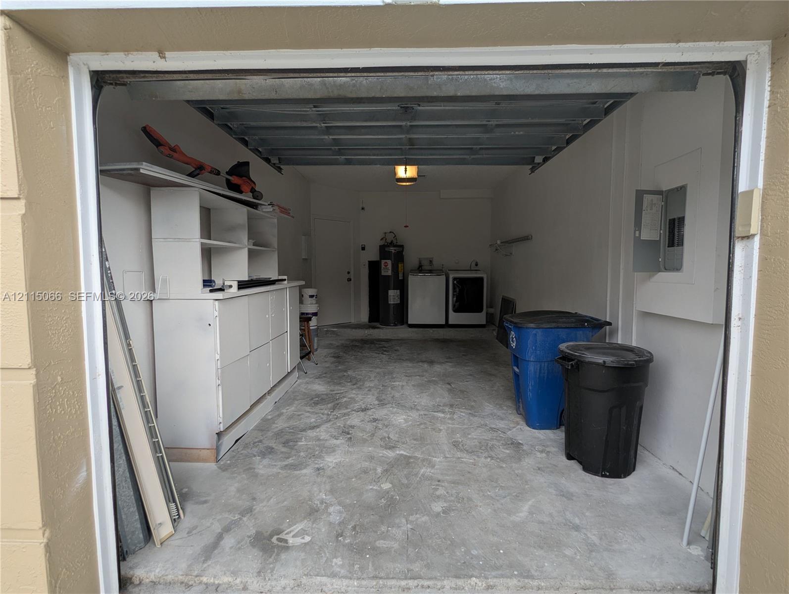Enclosed garage featuring concrete flooring, built-in white storage cabinetry, an overhead garage door, and dedicated utility connections