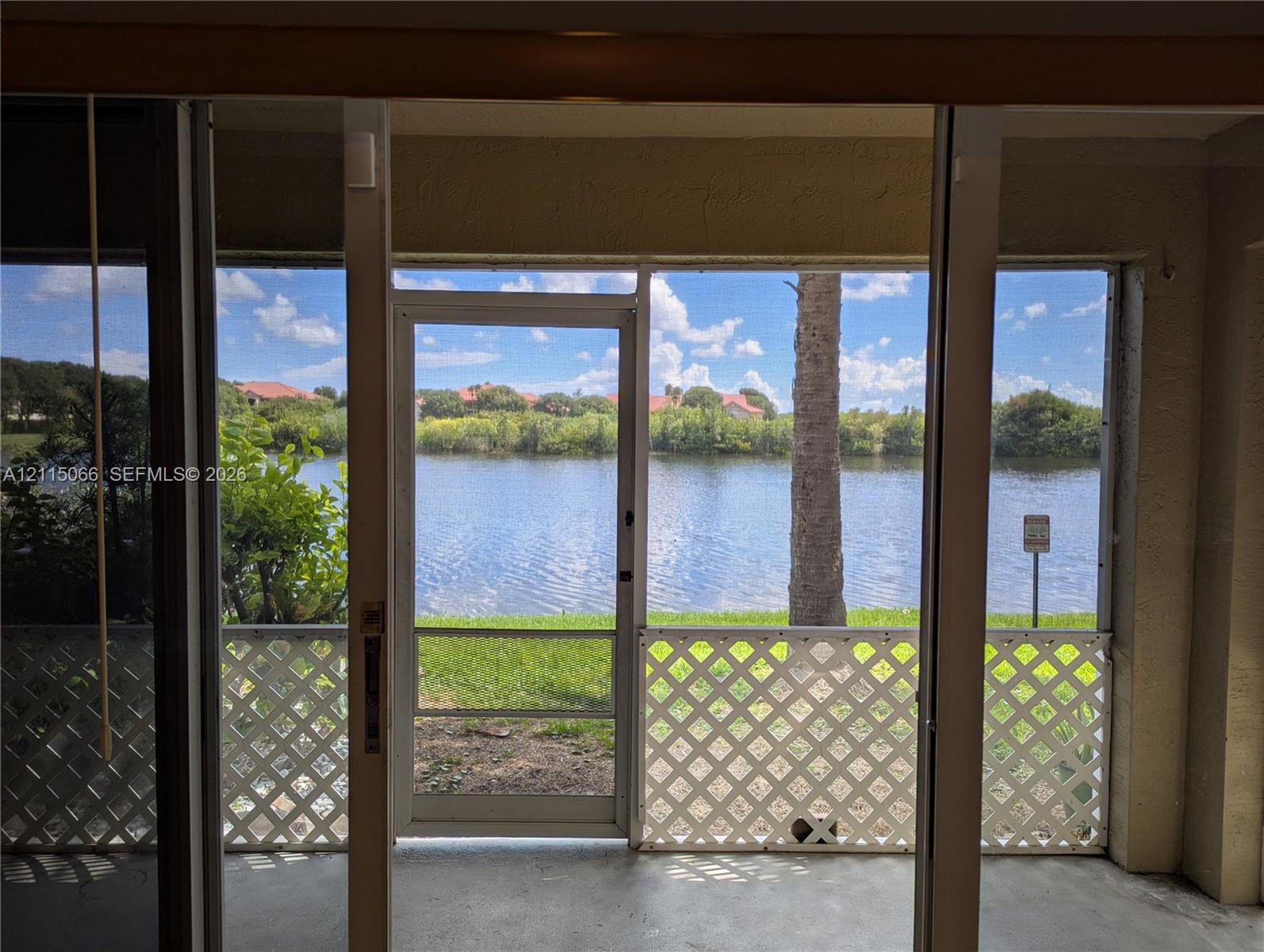 Screened-in patio featuring a concrete floor, white lattice wall panels, and a swinging screen door, oriented toward a pond