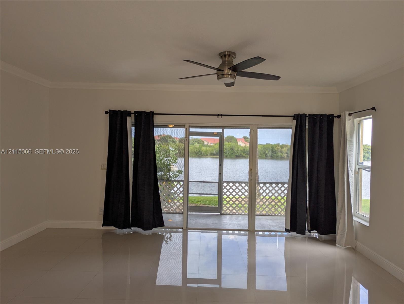 Living area featuring large-format tile flooring, a brushed-nickel ceiling fan, and sliding glass doors opening to a screened-in porch with water scenery