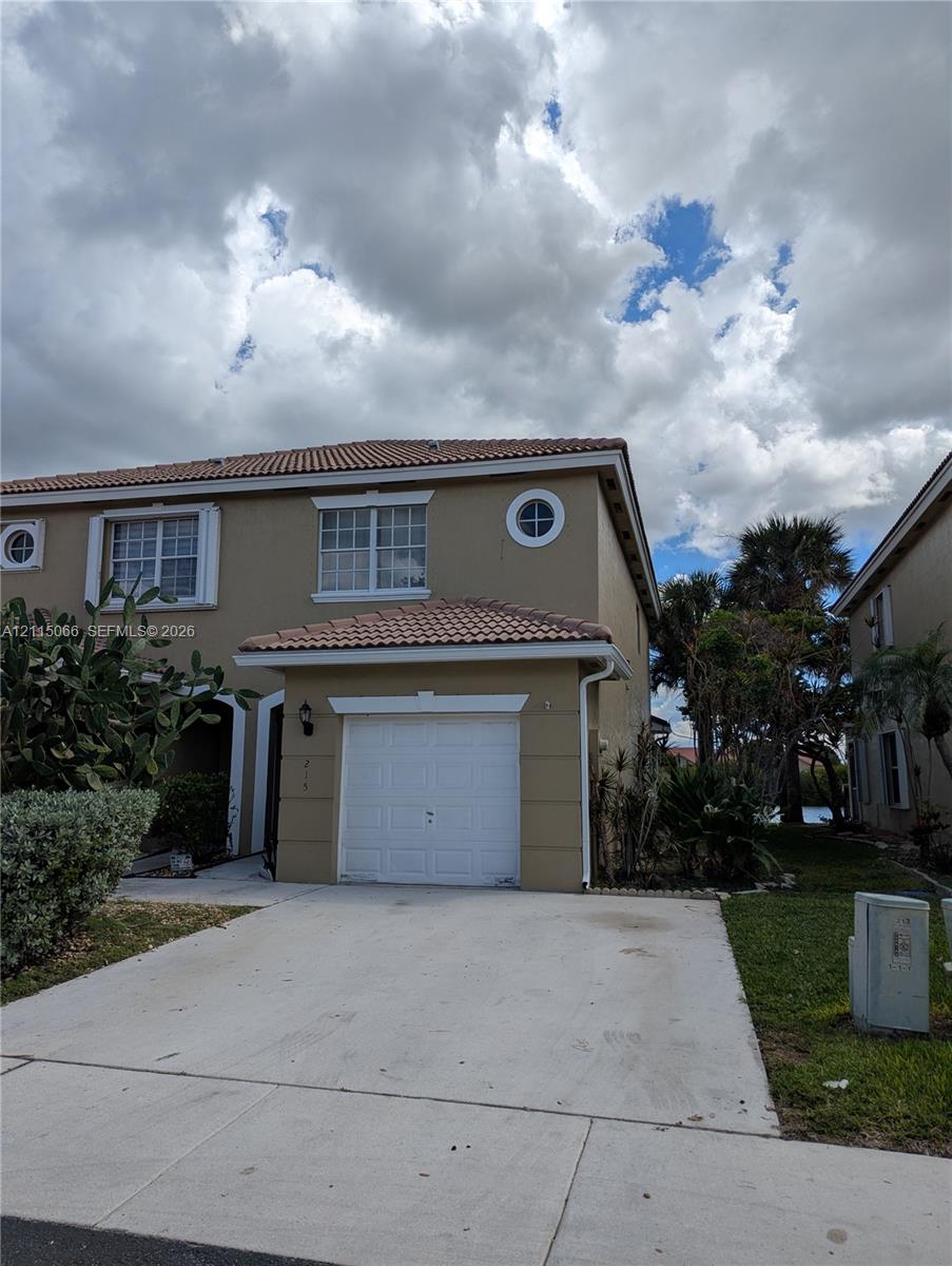 Two-story exterior featuring a tile roof, single-car garage, concrete driveway, and decorative round accent windows Two-story exterior featuring a tile roof, single-car garage, concrete driveway, and decorative round accent windows