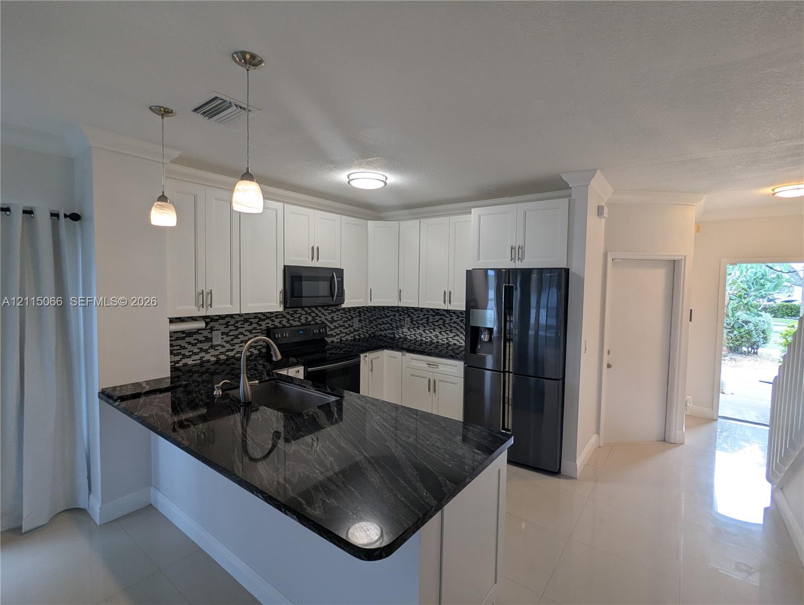 Kitchen featuring white shaker-style cabinetry, black stone countertops, decorative tile backsplash, dark-finish appliances, and dual pendant lighting
