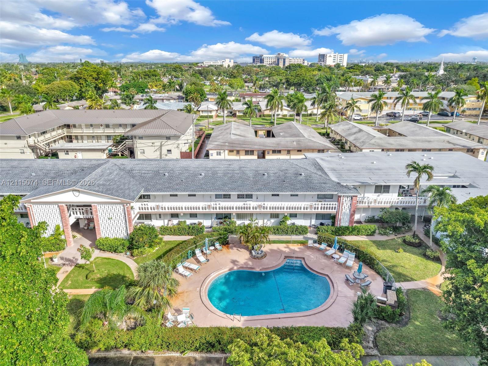Aerial perspective of a multi-story residential complex featuring a central swimming pool, paved pool deck, manicured landscaping with palm trees, and structural brick accents Aerial perspective of a multi-story residential complex featuring a central swimming pool, paved pool deck, manicured landscaping with palm trees, and structural brick accents