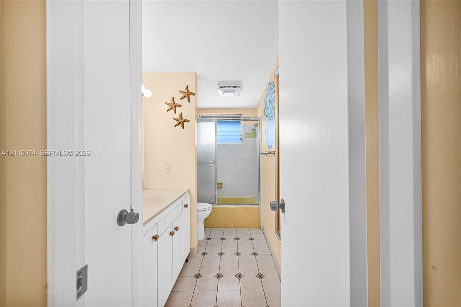 Bathroom featuring a vanity with integrated sink, white cabinetry, a glass-enclosed shower, and tile flooring with decorative inlay