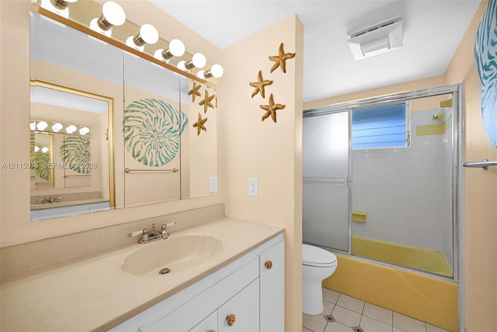Bathroom featuring a white vanity cabinet with an integrated sink, a large wall-to-wall mirror, multi-bulb overhead lighting, and a tub-shower combination with a sliding glass door