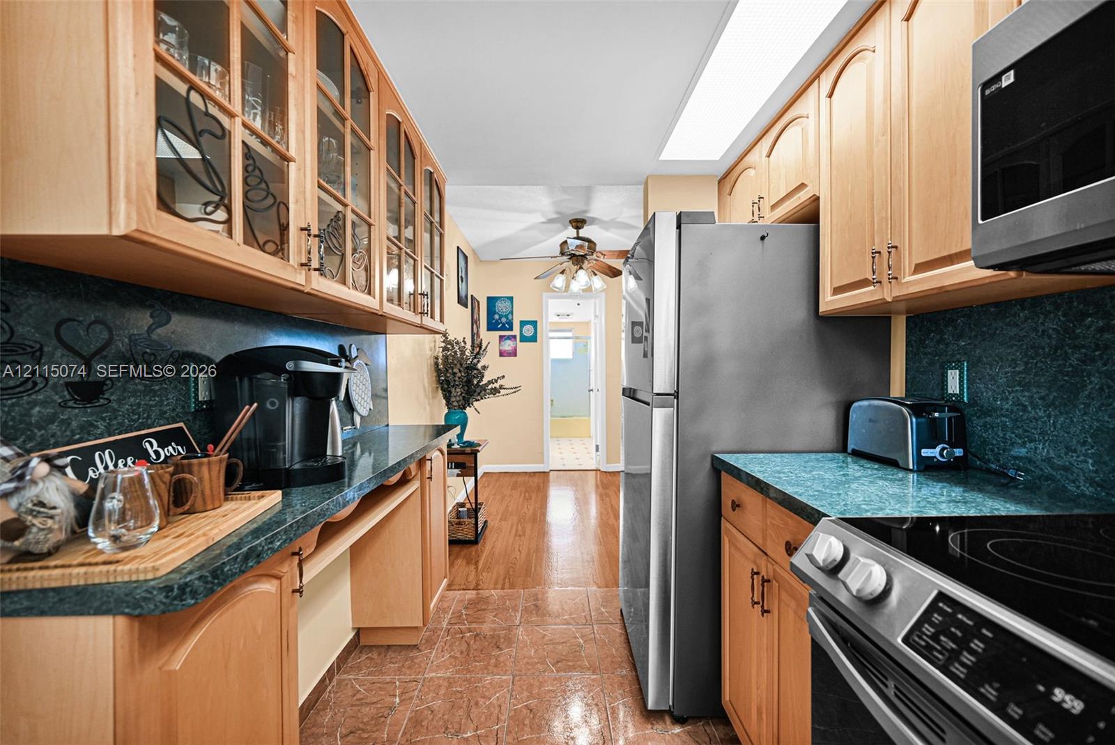Kitchen featuring light wood cabinetry with glass-front uppers, teal countertops, stainless steel appliances, and tiled flooring