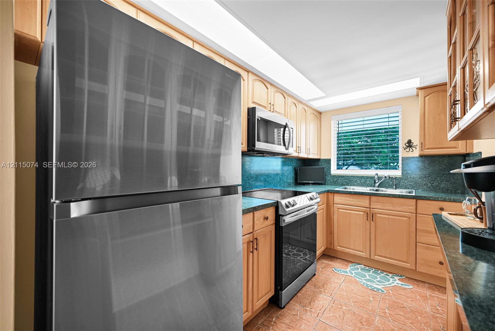 Kitchen featuring light wood cabinetry, stone-finish countertops, stainless steel appliances, a double-basin sink, and tile flooring
