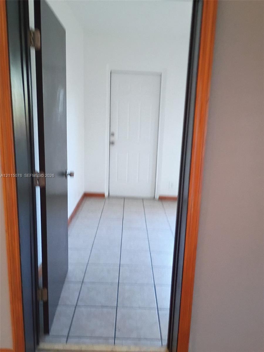 Square tile flooring, white six-panel door, and natural wood-finish door casing