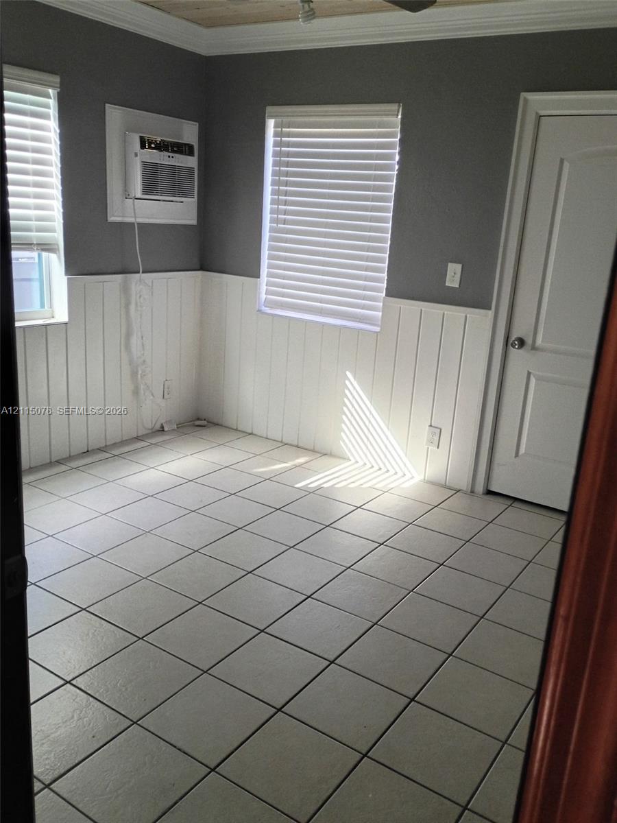 Interior space featuring square tile flooring, white vertical wainscoting, two windows with horizontal blinds, and a paneled interior door