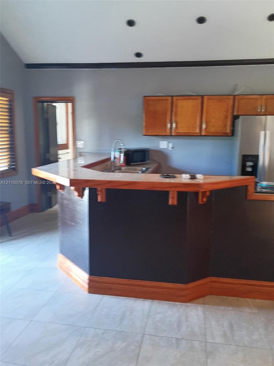 Kitchen featuring a tiered wood-topped breakfast bar, recessed ceiling lighting, wood-finish upper cabinetry, and light-toned tile flooring
