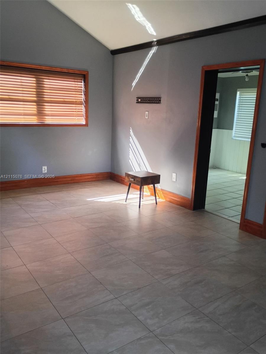Vaulted ceiling, large-format tile flooring, and natural wood-finish window and doorway casing