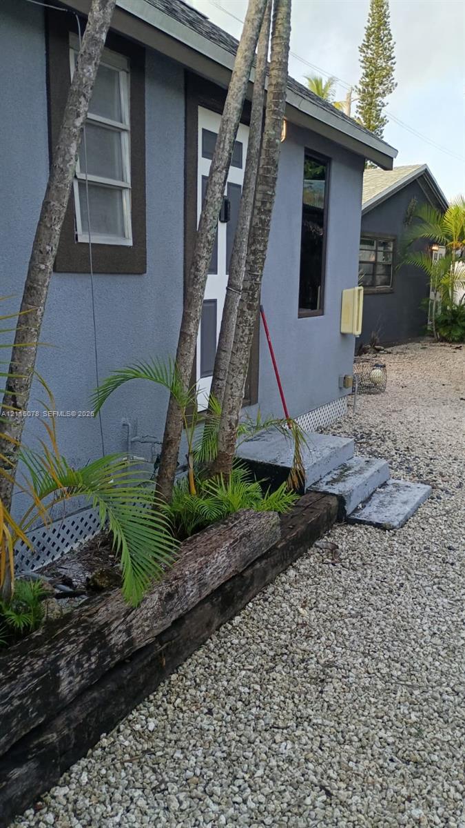 Exterior featuring stucco siding, timber-rail landscaping borders, concrete step entry, and gravel ground cover