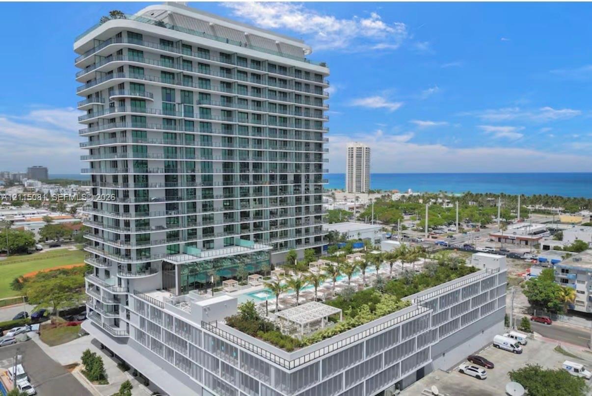 High-rise residential tower featuring a glass-facade exterior, wrap-around balconies, and an elevated terrace level with an outdoor pool, manicured landscaping, and pergolas High-rise residential tower featuring a glass-facade exterior, wrap-around balconies, and an elevated terrace level with an outdoor pool, manicured landscaping, and pergolas