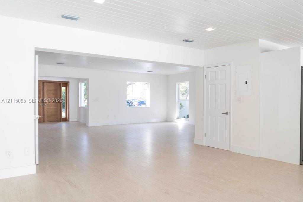 Open-concept interior featuring light-toned porcelain tile flooring, tongue-and-groove wood-finish ceiling, recessed lighting, and a six-panel interior door