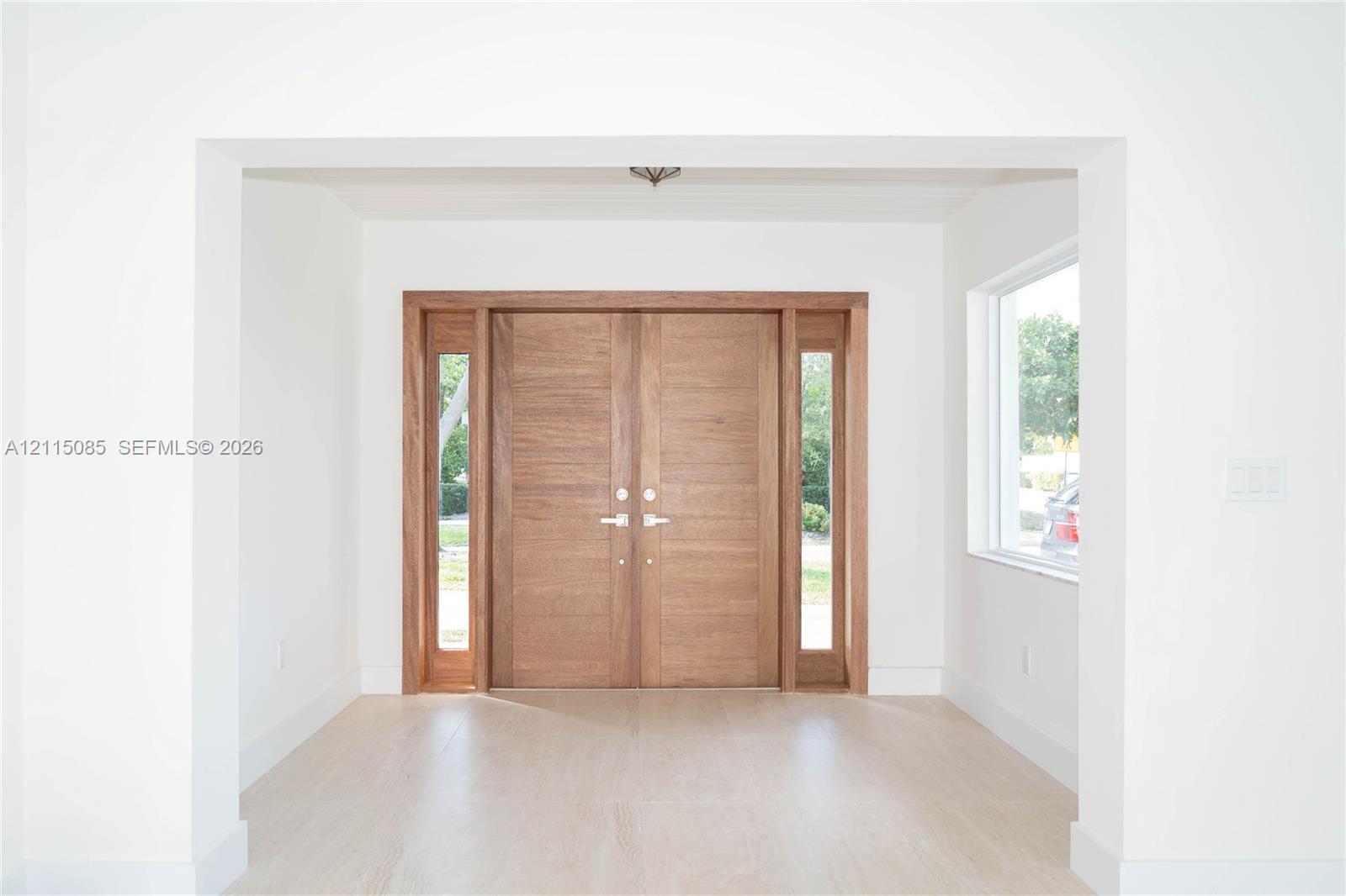 Double entry doors featuring wood-grain finish, integrated sidelights, and brushed metallic hardware, complemented by light-toned porcelain tile flooring