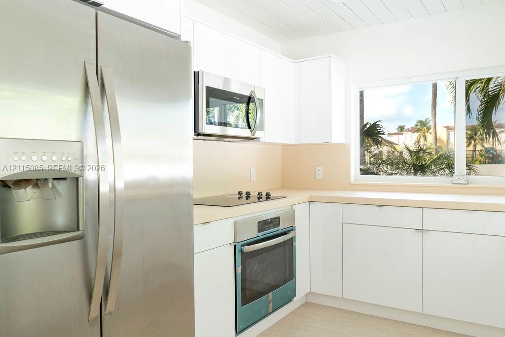 Kitchen featuring white cabinetry, stainless steel appliances, solid surface countertops, and a built-in cooktop