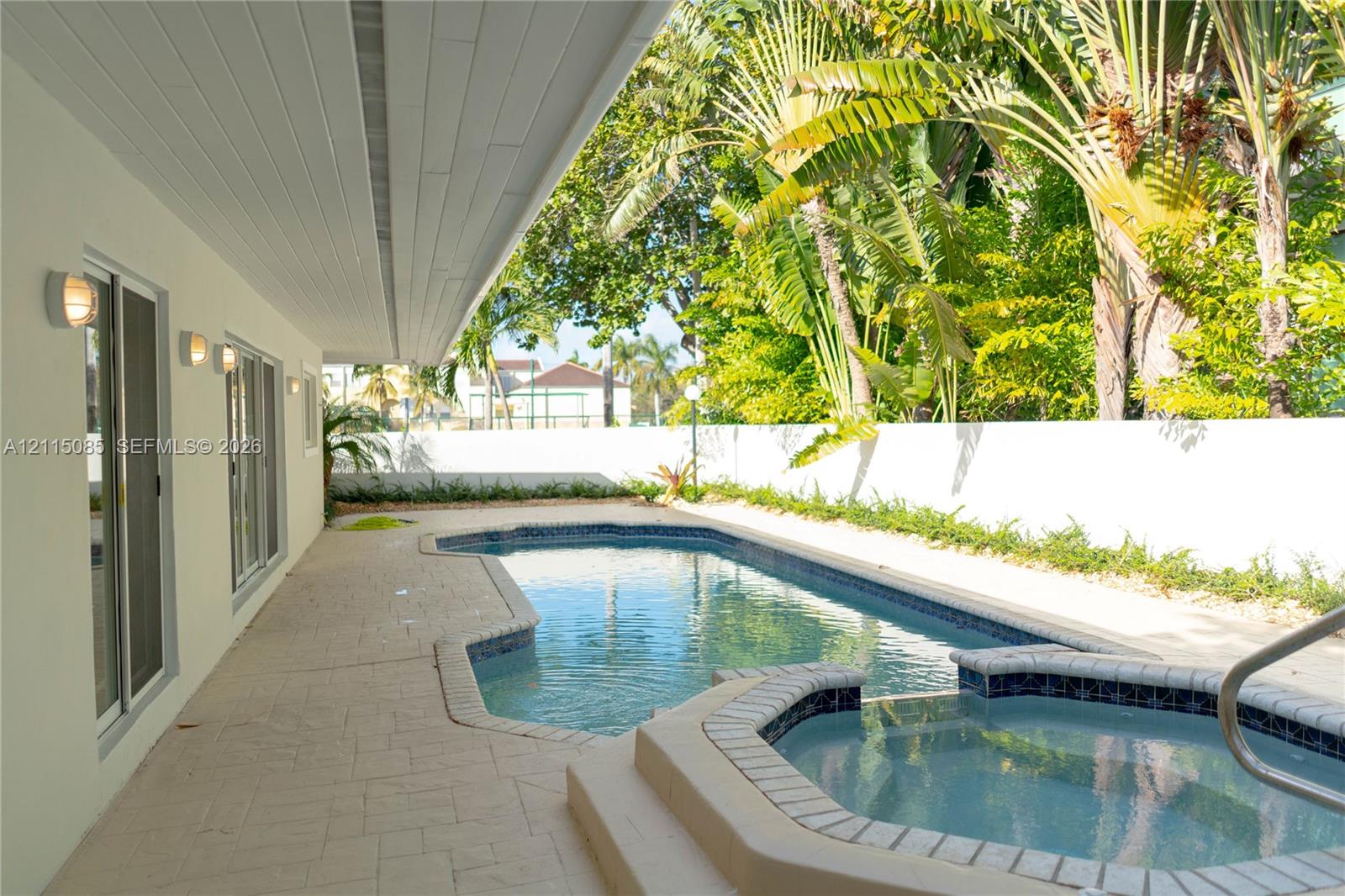 Covered patio featuring stone-tiled flooring, swimming pool with tiled coping, integrated spa, and surrounding privacy wall