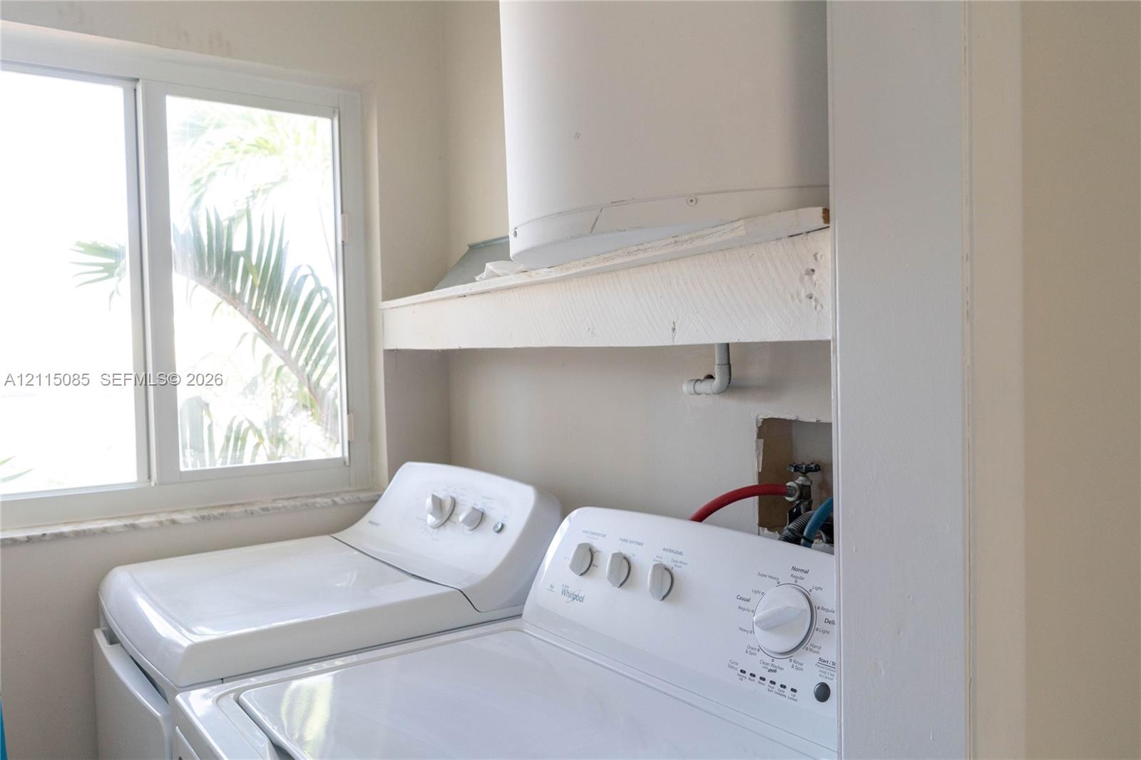 Laundry area featuring white top-load washer and dryer, horizontal built-in shelving, and a large sliding window with stone-finish sill