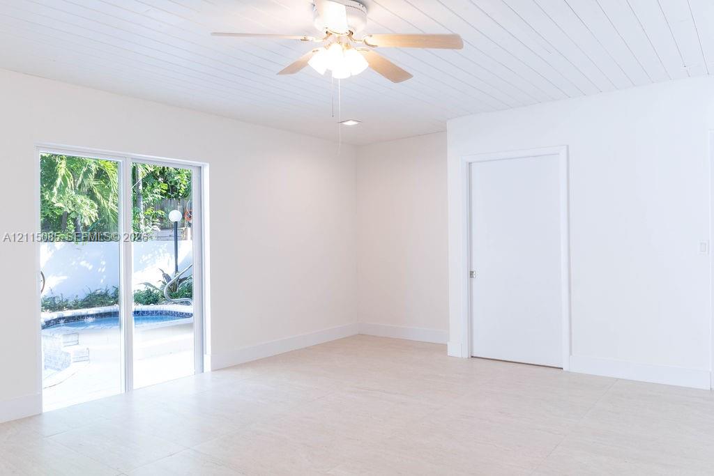 Interior space featuring light-toned porcelain tile flooring, beadboard ceiling, ceiling fan with integrated lighting, and sliding glass door with exterior pool access