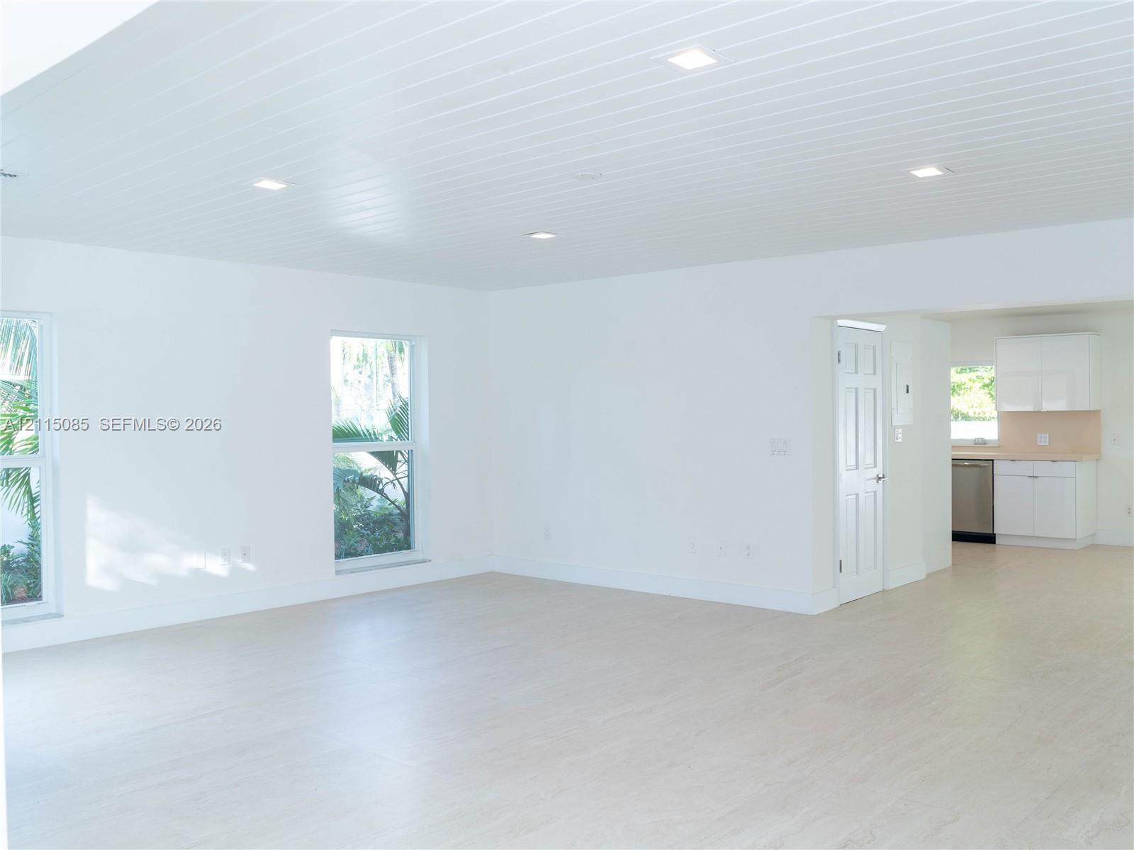 Open-concept interior featuring light-toned porcelain tile flooring, tongue-and-groove ceiling with recessed lighting, double-hung windows, and white cabinetry