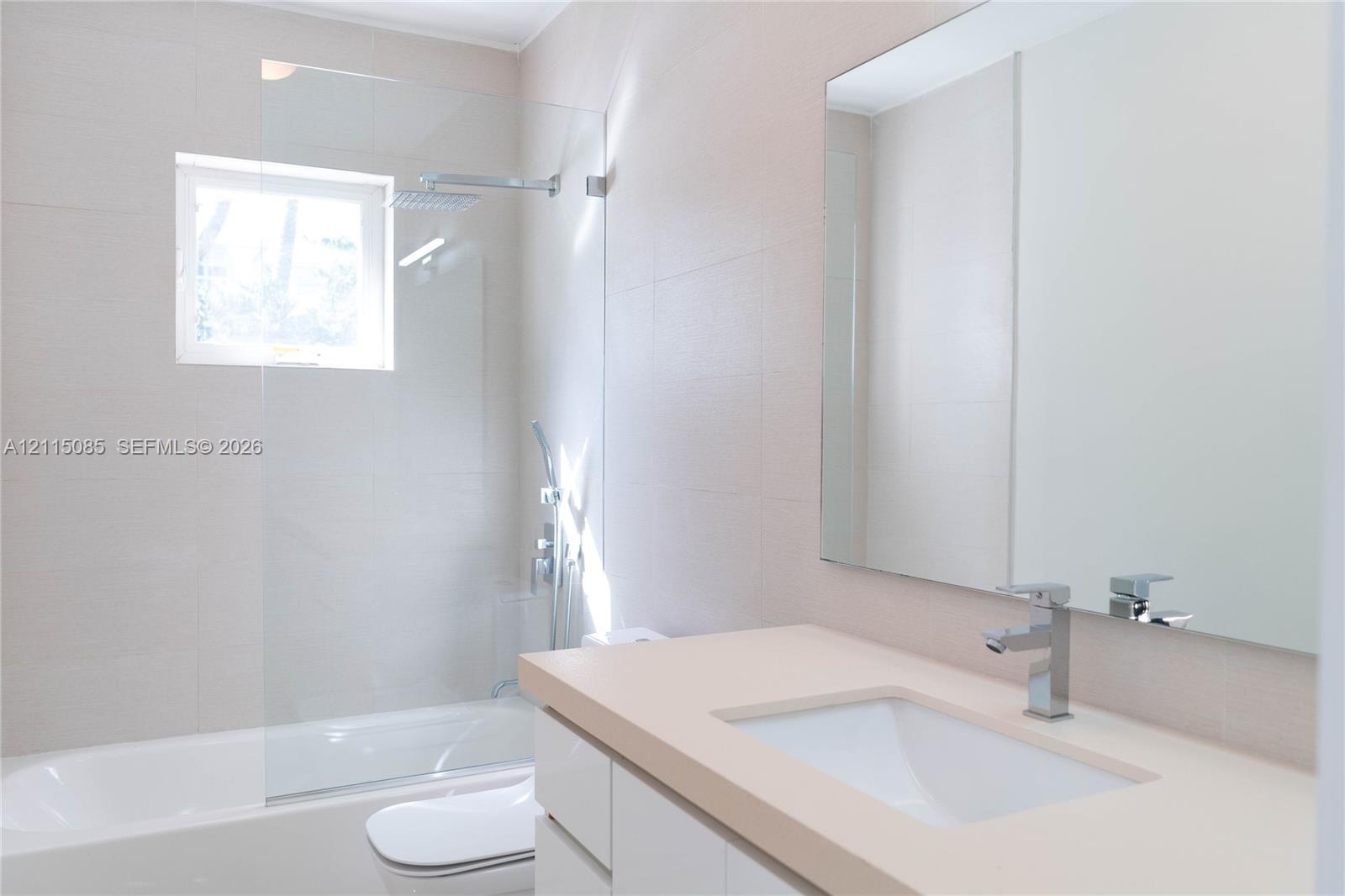 Bathroom featuring a white vanity with a solid surface countertop, an undermount sink, a frameless glass shower partition, wall-mounted shower hardware, and a large plate glass mirror