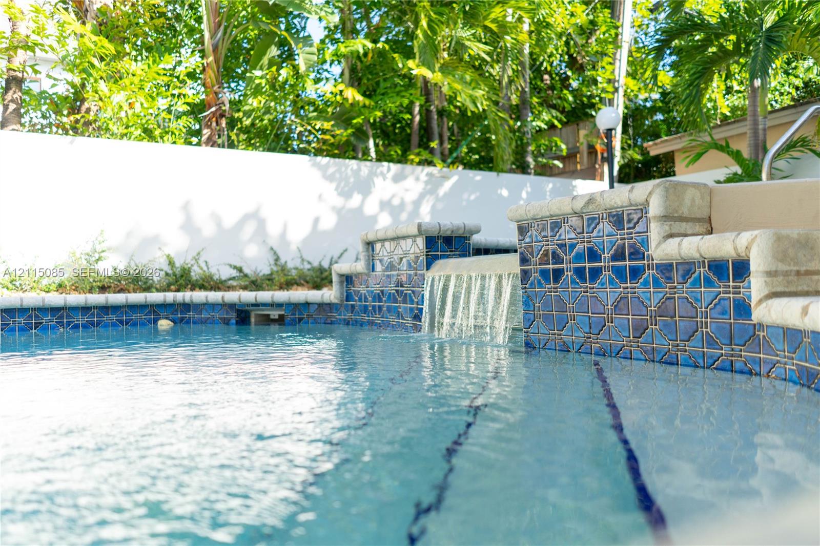 Swimming pool featuring decorative blue tiled accents, a built-in water feature, tiered pool steps, and a solid perimeter privacy wall