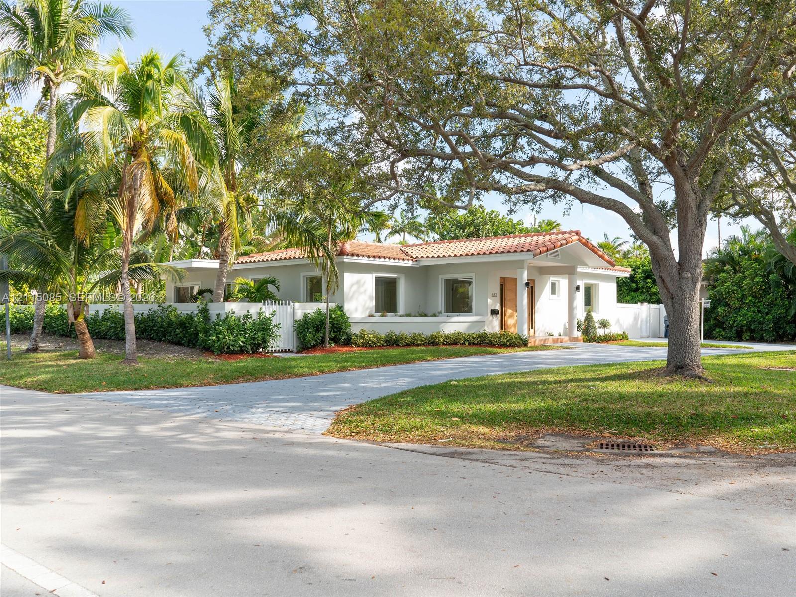 Single-story residence featuring a tile roof, paved driveway, enclosed perimeter wall, and mature landscaping
