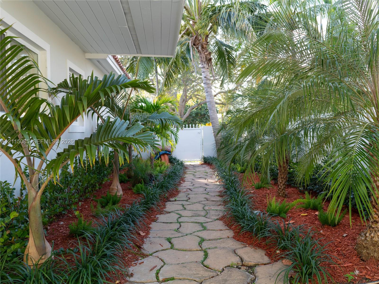 Flagstone walkway bordered by mature palm trees and manicured landscape beds with red mulch