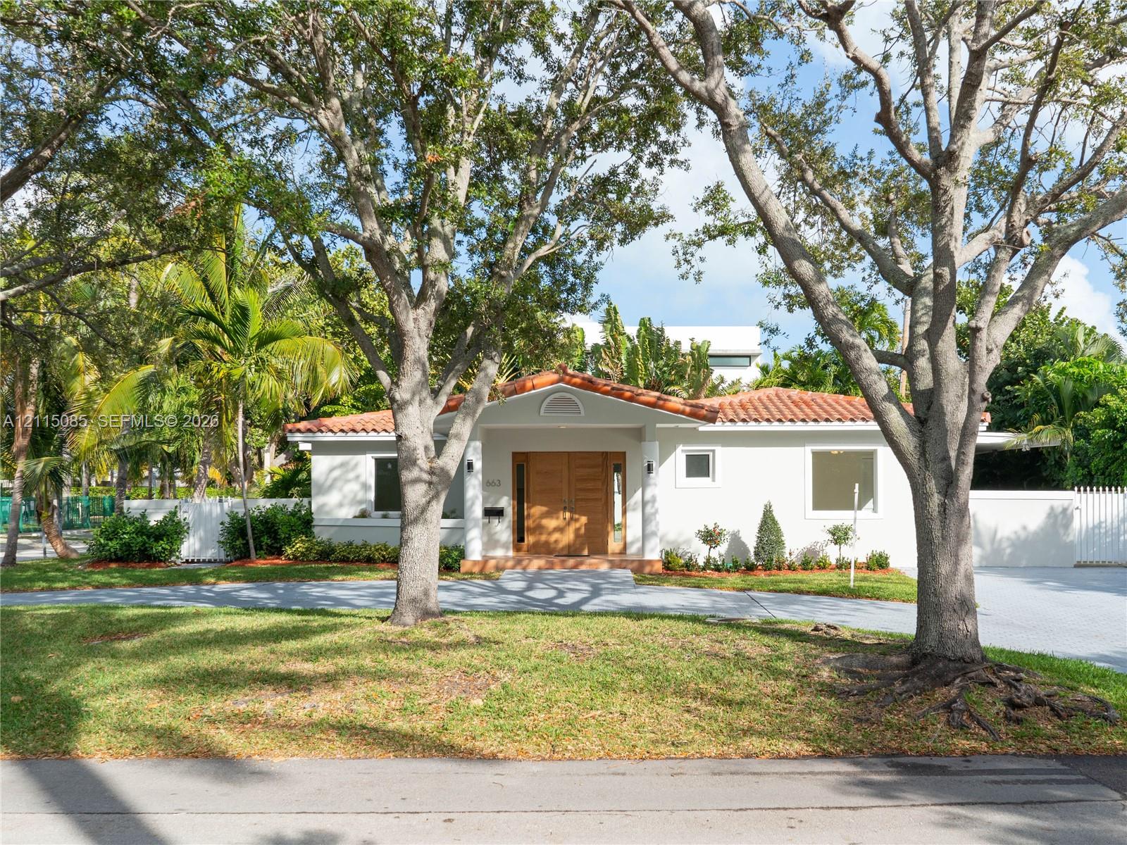 Stucco exterior featuring a terracotta tile roof, wood-finish double front doors, and a paver driveway