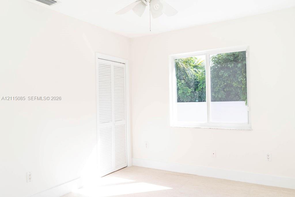 Neutral-toned room featuring a white dual-pane sliding window, closet with white louvered doors, and a ceiling-mounted fan