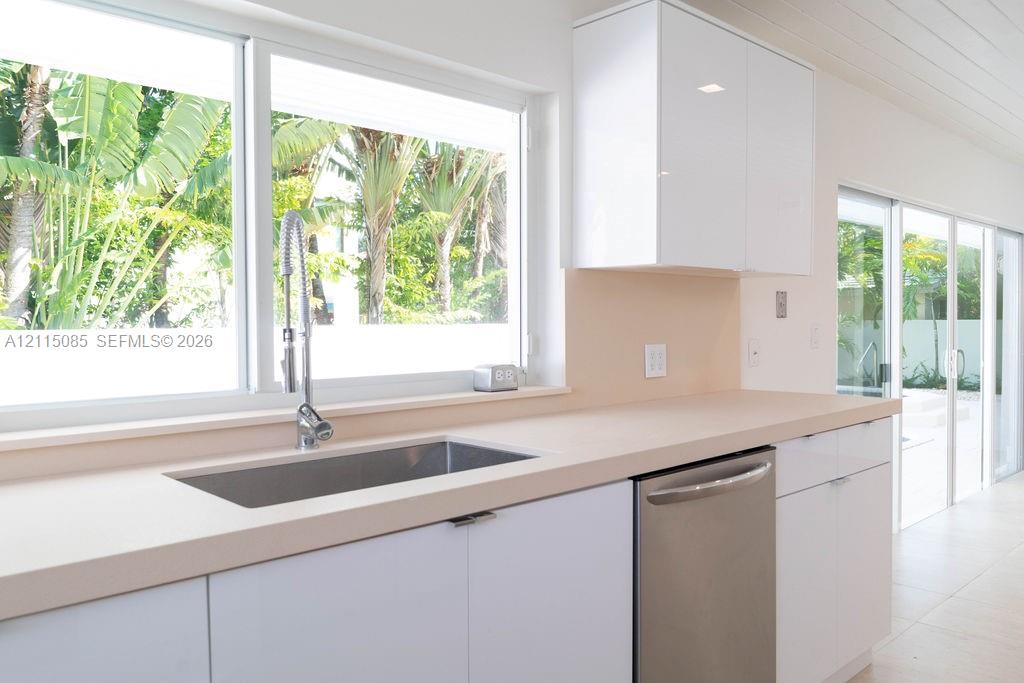 Kitchen featuring white high-gloss cabinetry, stone-surface countertops, a stainless steel undermount sink with a gooseneck faucet, integrated stainless steel dishwasher, and sliding glass doors