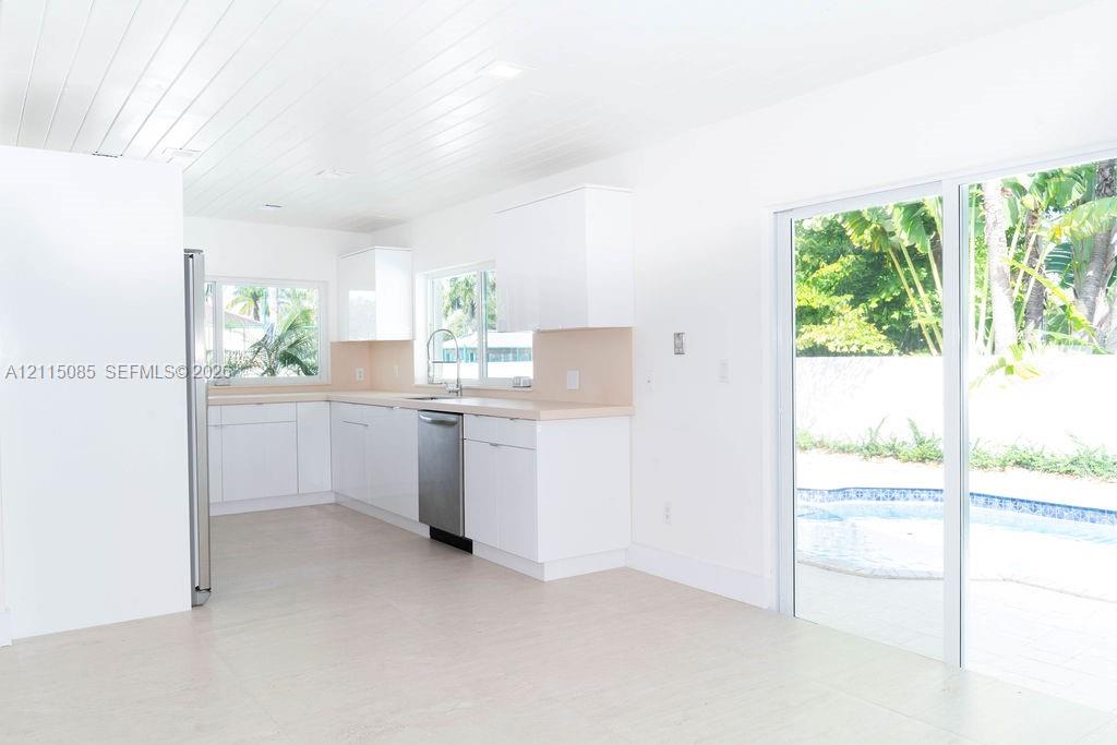 Kitchen featuring white cabinetry, solid-surface countertops, stainless steel dishwasher, tongue-and-groove plank ceiling, and sliding glass doors