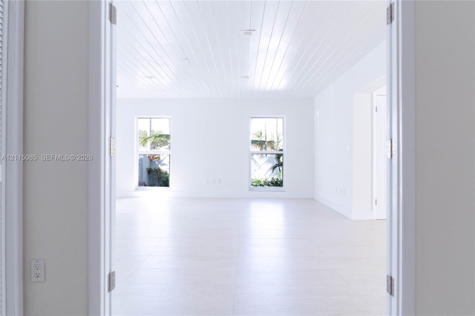 Plank-style ceiling, light-toned porcelain tile flooring, and dual picture windows