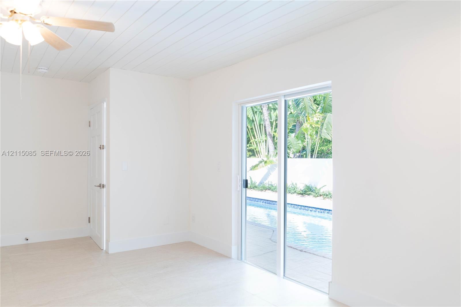 Room featuring a beadboard ceiling, light-toned porcelain tile flooring, ceiling fan with integrated lighting, and sliding glass doors with direct exterior access to a pool