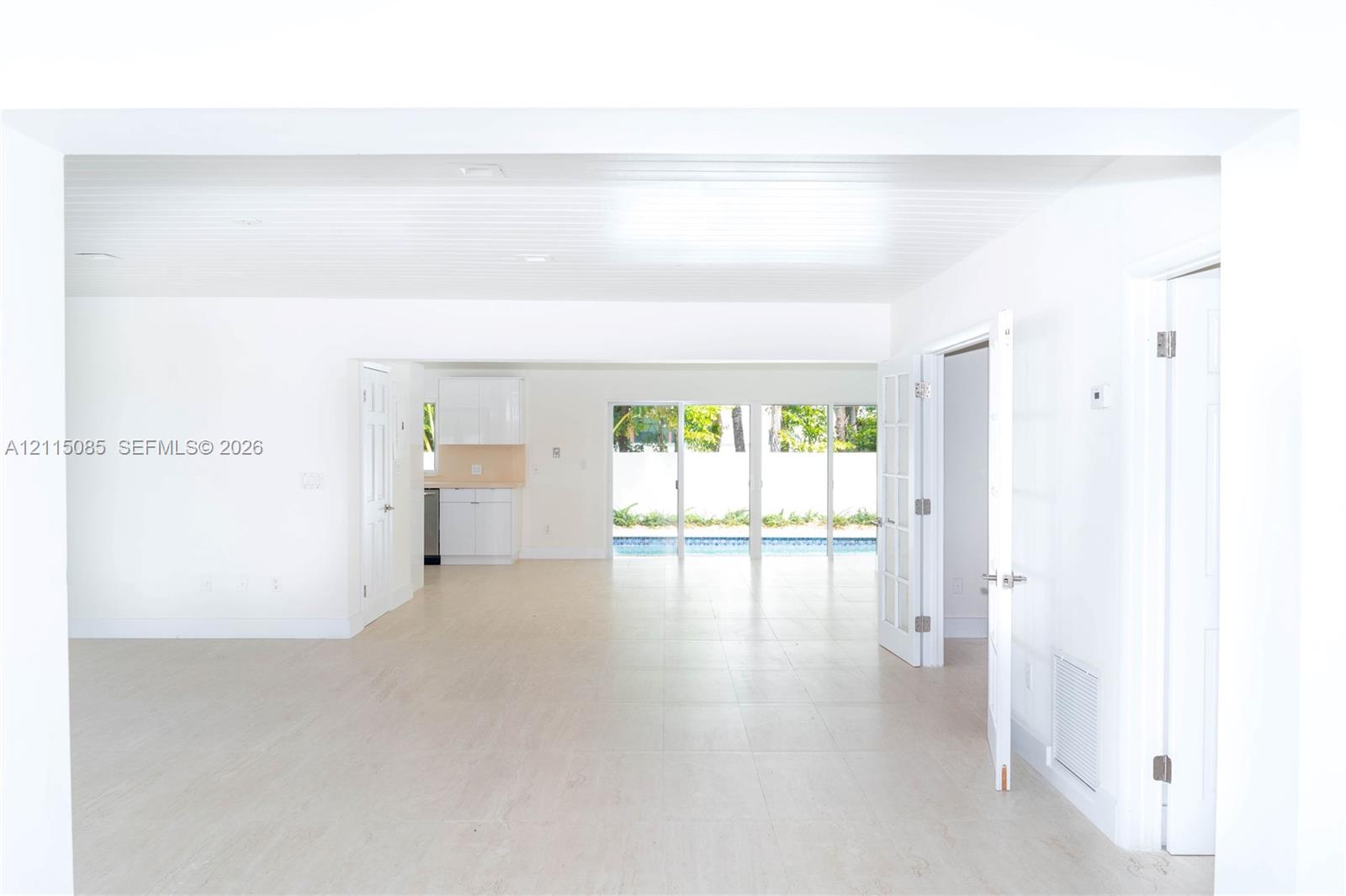 Open-concept interior featuring light-toned porcelain tile flooring, recessed ceiling lighting, glass sliding doors, and white cabinetry