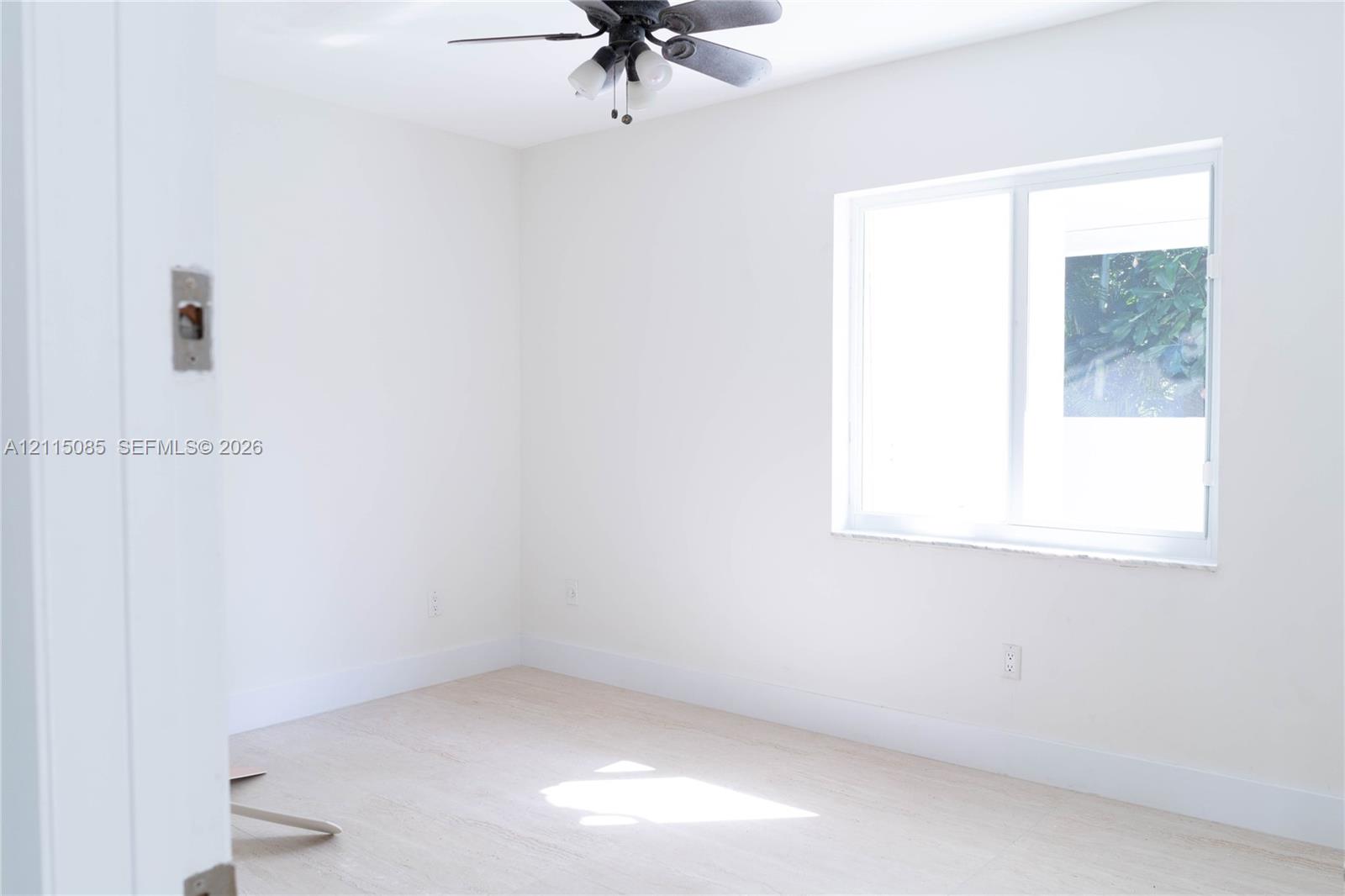 Neutral interior space featuring light-toned porcelain tile flooring, a ceiling fan with integrated lighting, and a sliding window