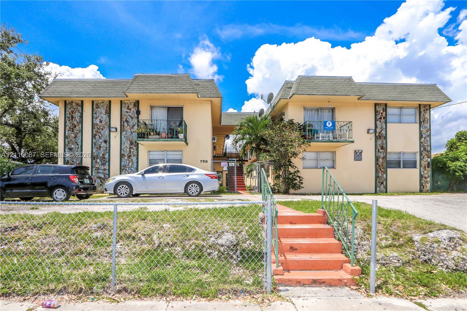 Two-story building exterior featuring textured stone accents, metal balcony railings, and a concrete staircase with metal handrails Two-story building exterior featuring textured stone accents, metal balcony railings, and a concrete staircase with metal handrails