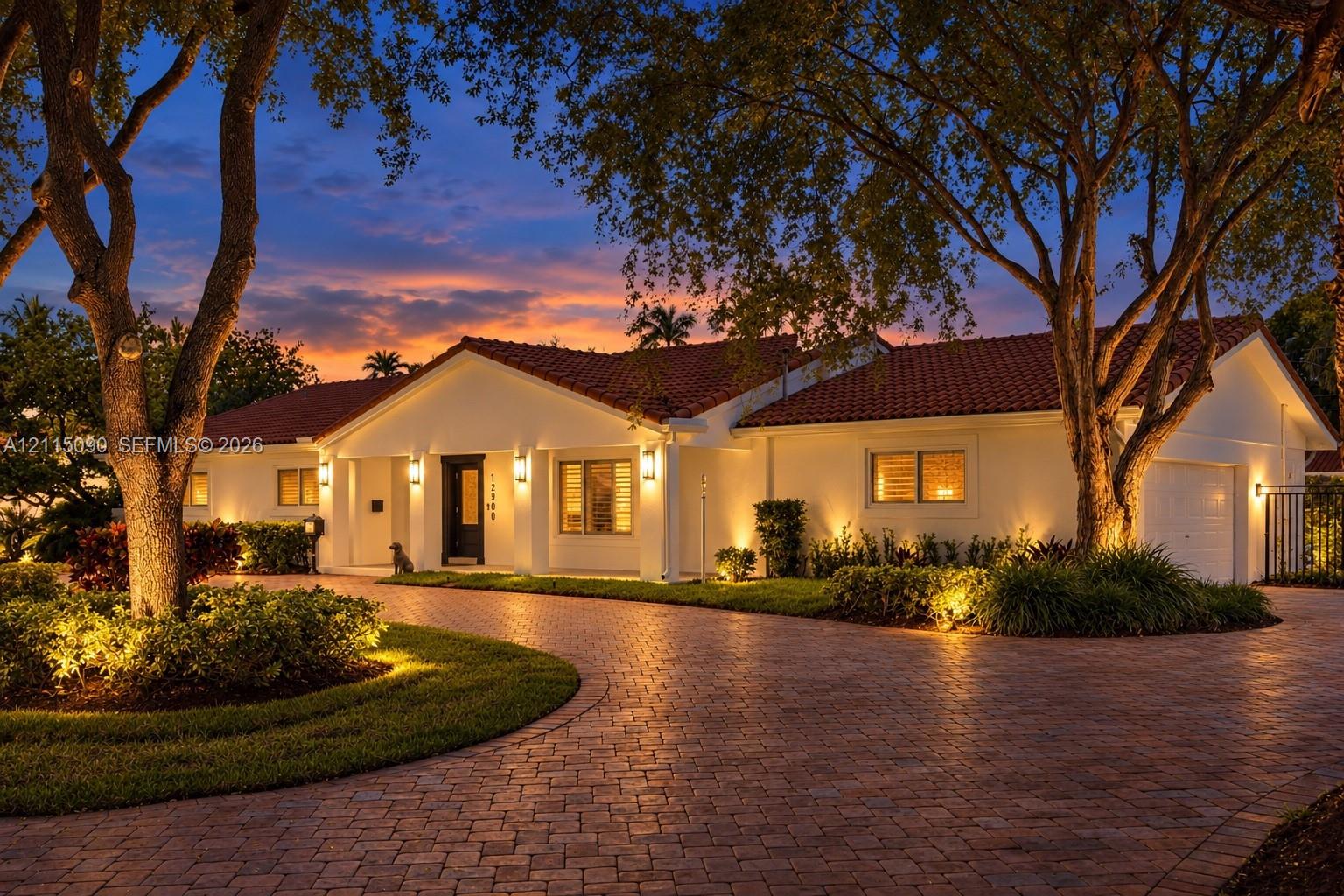Single-story residence featuring a tile roof, light-toned exterior finish, and a brick-paver circular driveway surrounded by mature landscaping Single-story residence featuring a tile roof, light-toned exterior finish, and a brick-paver circular driveway surrounded by mature landscaping