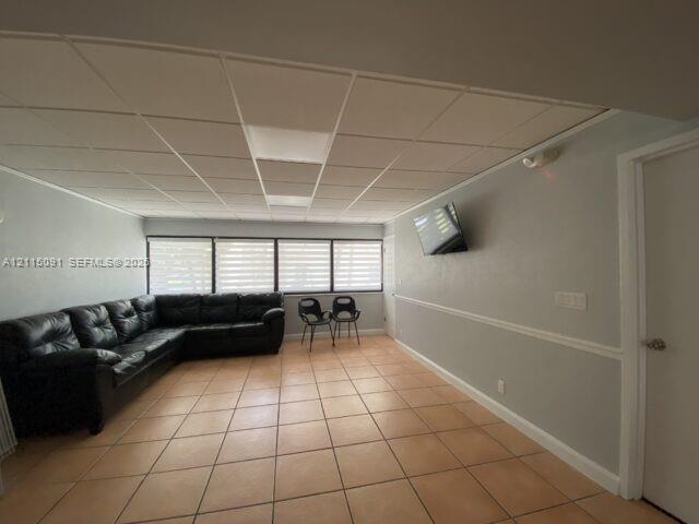 Interior space featuring ceramic tile flooring, a grid-patterned drop ceiling, and large windows with horizontal blinds