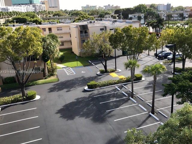 Asphalt parking lot featuring designated stall markings, mature trees, landscaped shrubbery, and pole-mounted exterior lighting