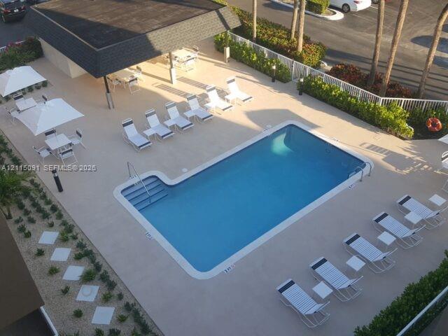 Outdoor swimming pool with built-in steps, covered patio structure, perimeter landscaping, and concrete decking
