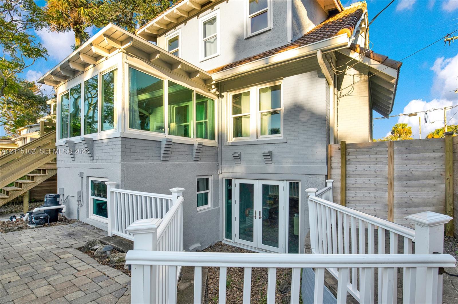 Painted brick exterior featuring an expansive sunroom with wrap-around windows, paved patio, double-door glass entrance, and white railing enclosures