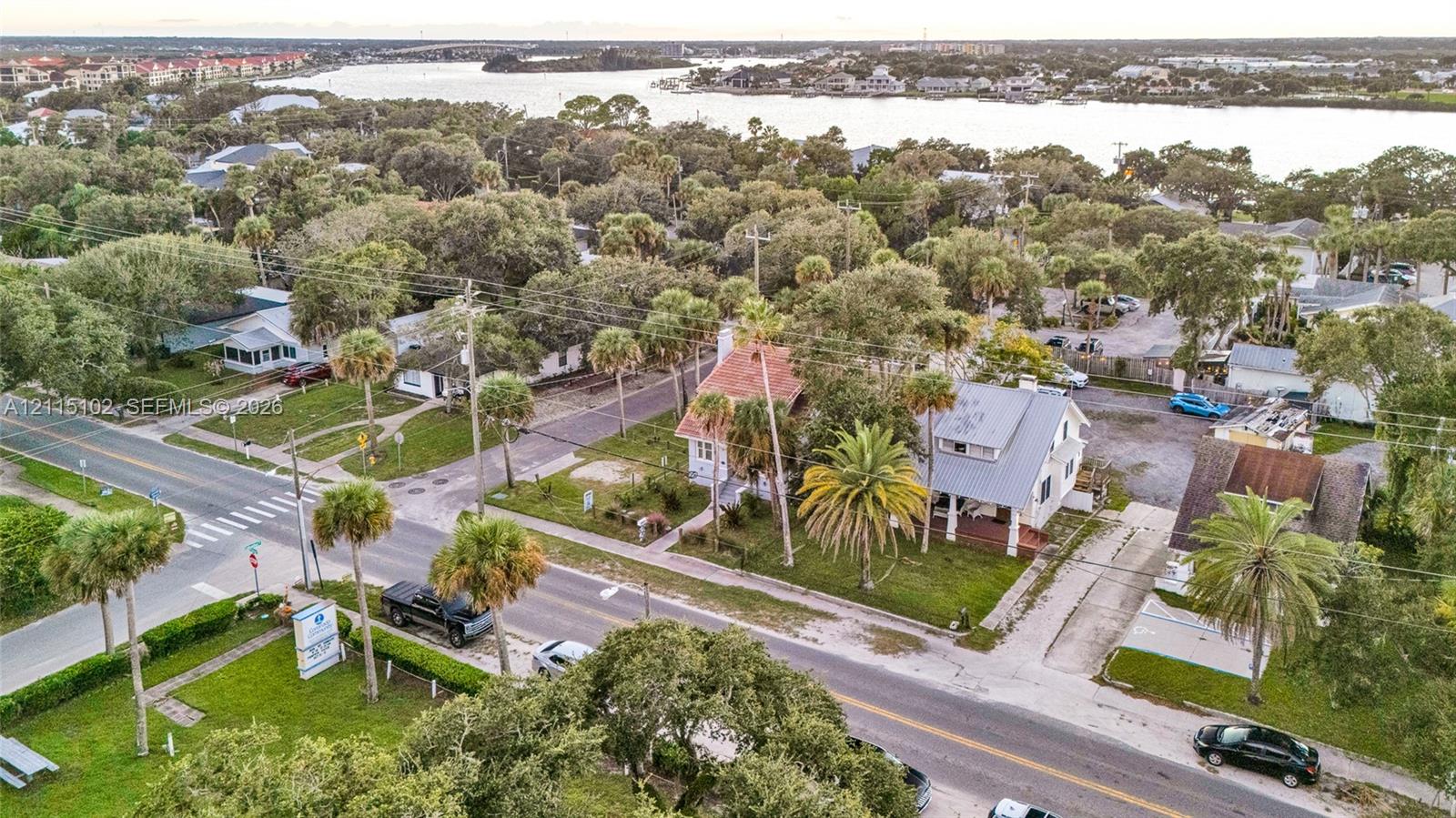 Aerial perspective of the property featuring mature landscaping, palm trees, and proximity to the waterfront