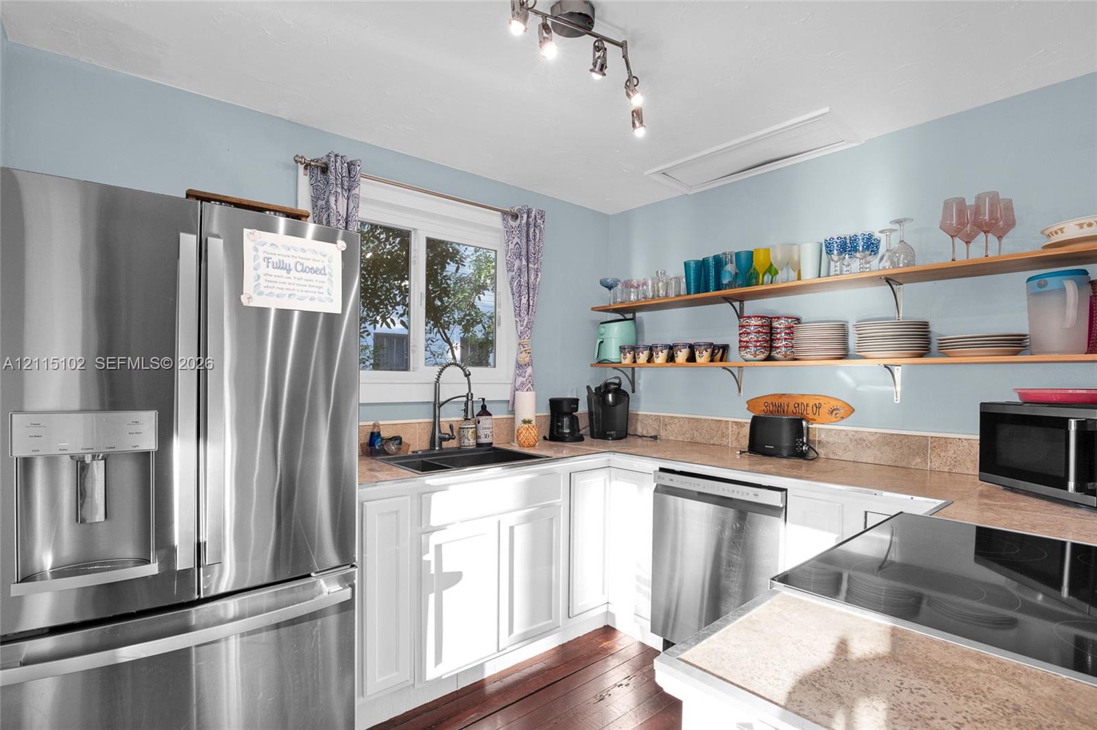 Kitchen featuring stainless steel appliances, white cabinetry, wood-finish flooring, stone-surface countertops, and wall-mounted shelving