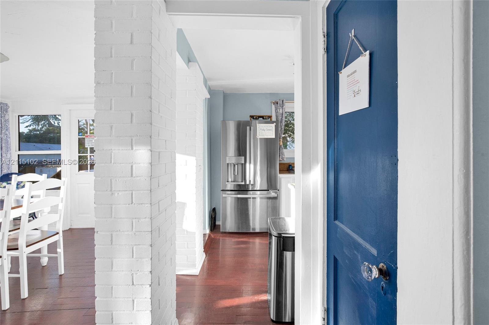 Interior space featuring a white-painted brick structural column, wood-finish flooring, and a blue-painted solid wood door with a glass knob
